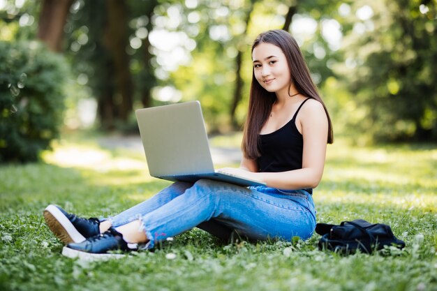 Aziatische student of freelance vrouw die laptop op treden in universitaire campus of modern park met behulp van. Informatietechnologie, onderwijs of informeel bedrijfsconcept.