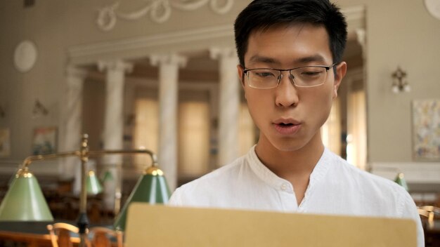 Aziatische student opent spannend envelop met examenresultaten in universiteitsbibliotheek