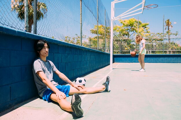 Aziatische tienerstudent die naast sportsgroundomheining rusten