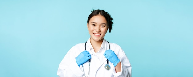 Gratis foto aziatische vrouw arts verpleegster glimlachend zelfverzekerd aanpassen van stethoscoop op nek staande in medisch uniform