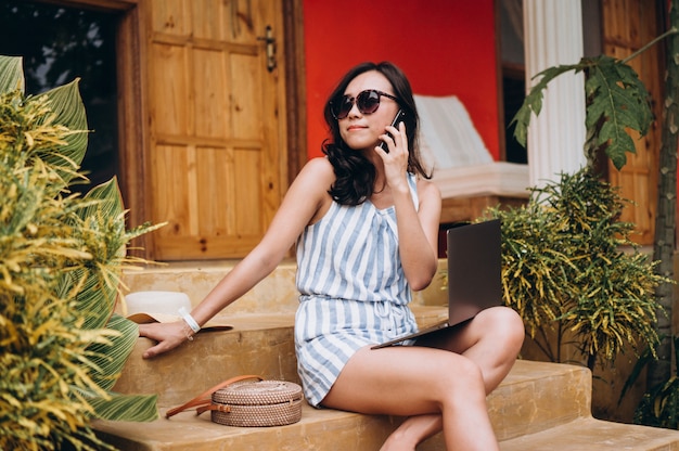 Aziatische vrouw die aan laptop op een vakantie werkt en op de treden zit