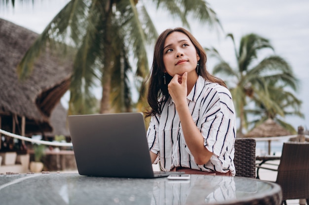 Aziatische vrouw die aan laptop op een vakantie werkt