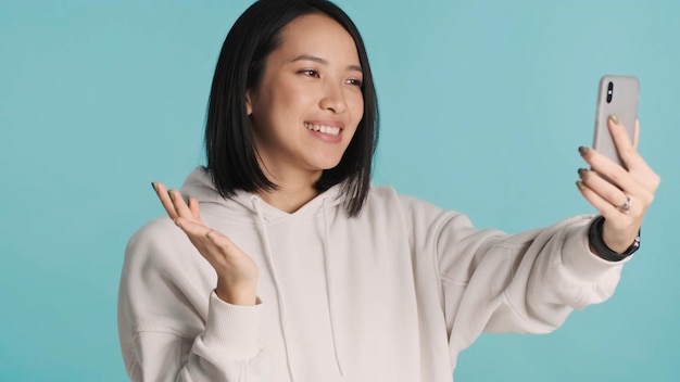 Aziatische vrouw die een videogesprek maakt met een smartphone die er gelukkig uitziet geïsoleerd op een kleurrijke achtergrond Gesprek op afstand