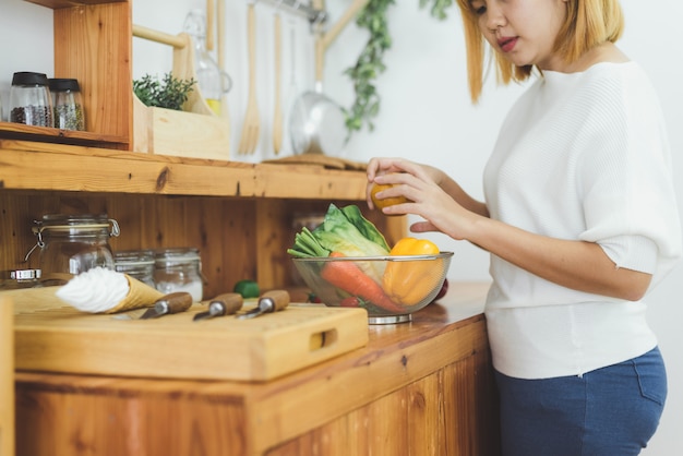 Aziatische vrouw die gezond voedsel maken die zich het gelukkige glimlachen in keuken bevinden die salade voorbereiden