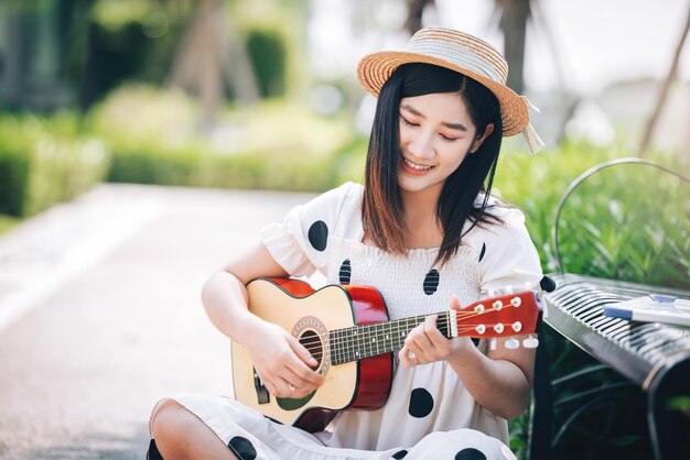 Aziatische vrouw die gitaar speelt in het parklevensstijl en recreatieconcept