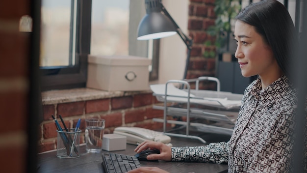 Aziatische vrouw die naar de monitor kijkt om aan een zakelijk project te werken, een marketingstrategie op de computer plant. Close up van ondernemer met behulp van technologie, werken aan financiële groei. Uit de hand geschoten