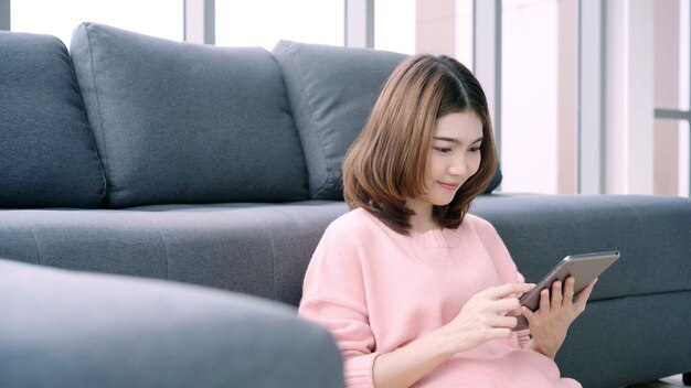 Aziatische vrouw die tablet gebruiken terwijl het liggen op huisbank in haar woonkamer.