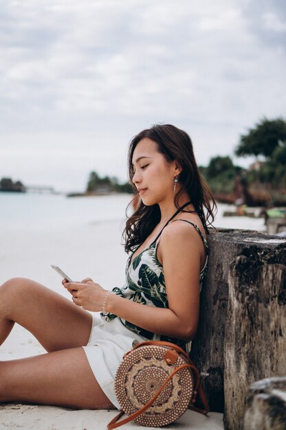 Aziatische vrouw die telefoon gebruikt bij het strand op een vakantie