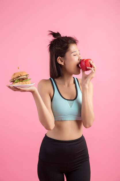 Aziatische vrouw die tussen hamburger en rode appel op roze kiest