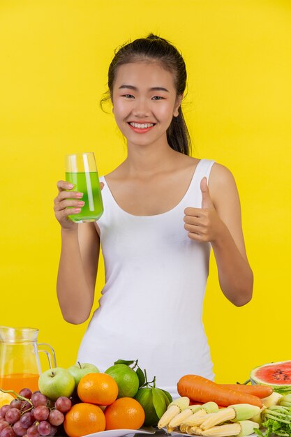 Aziatische vrouw Holdingapple glas met je rechterhand, en op de tafel zijn er veel fruit.