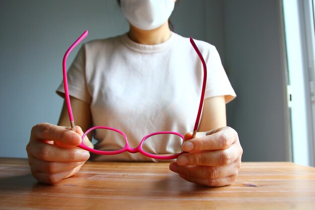 Aziatische vrouw met masker die een bril in de hand houdt tijdens de pauze van het werk