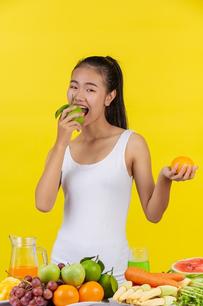 Aziatische vrouw met sinaasappels aan beide kanten, en op de tafel zijn er veel fruit.