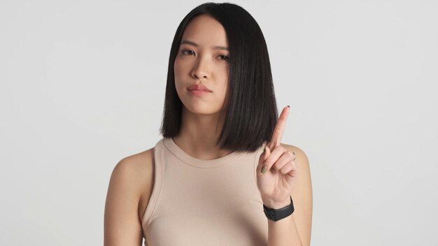 Aziatische vrouw ziet er zelfverzekerd uit en toont geen gebaar naar de camera op een witte achtergrond
