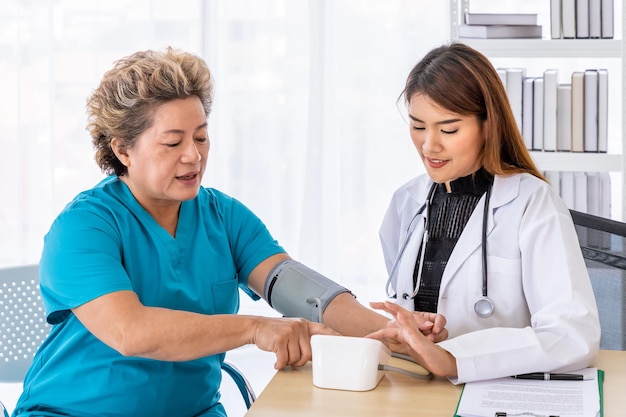 Aziatische vrouwelijke arts die de bloeddruk meet van een oudere oudere patiënt die naar de camera kijkt
