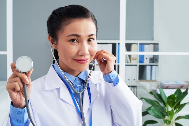 Aziatische vrouwelijke arts poseren met stethoscoop in kliniek