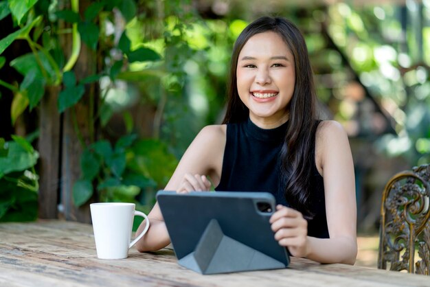 Aziatische vrouwelijke digitale nomade geluk vrijheid vrolijk lachend werken met behulp van tablet in tuin outdoorasia vrouw freelance ontspannen vrije tijd werken overal werken en reizen iwith tuin bokeh achtergrond