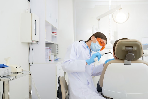 Aziatische vrouwelijke tandarts die de holte van de patiënt in kliniek behandelen
