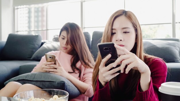 Aziatische vrouwen gebruikend smartphone en etend popcorn in woonkamer thuis, groep kamergenootvriend