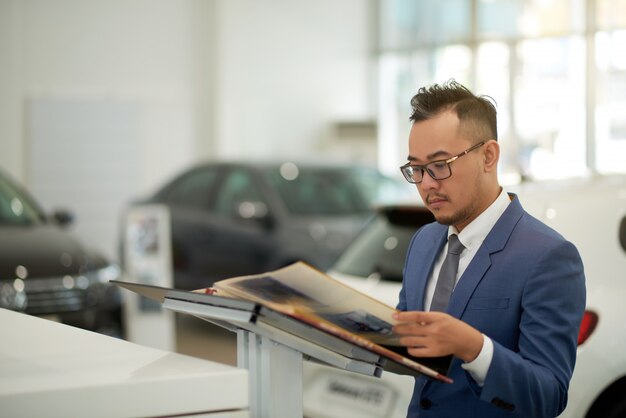 Aziatische zakenman die zich in de toonzaal van het autohandel drijven en door album kijken