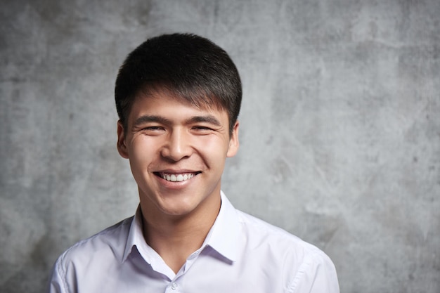 Aziatische zakenman toothy glimlachen. portret van een jonge aantrekkelijke kazachse student in een wit overhemd in de studio