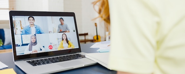 Aziatische zakenvrouw met behulp van laptop praten met collega's over plan in videogesprek vergadering terwijl u thuis werkt in de woonkamer. Zelfisolatie, sociale afstand nemen, quarantaine voor coronaviruspreventie.