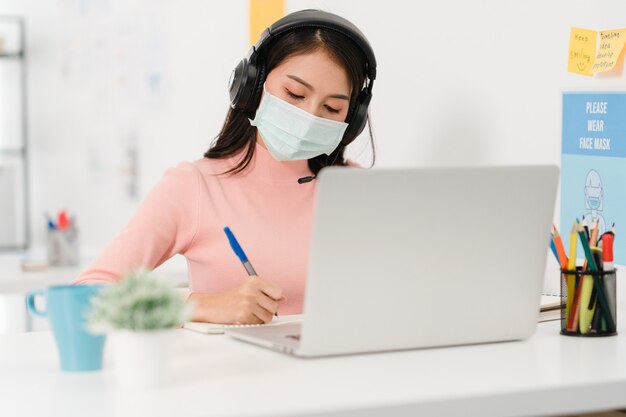 Aziatische zakenvrouw sociale afstand nemen in nieuwe normale situatie voor viruspreventie tijdens het gebruik van laptoppresentatie aan collega's over plan in videogesprek tijdens het werk op kantoor. Leven na het coronavirus.