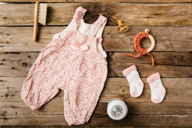 Baby&#39;s jurk; borstel; fopspeen; speelgoed en paar sokken met fles melk op houten tafel