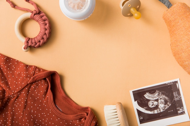 Baby&#39;s kleding; borstel; speelgoed; fopspeen; gevulde peer en echografie foto op een oranje achtergrond