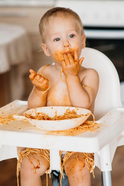 Babyjongen likt zijn vingers na het eten van pasta