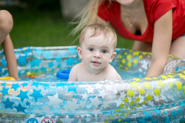 Babyjongen zwemmen in opblaasbaar zwembad in de tuin met moeder