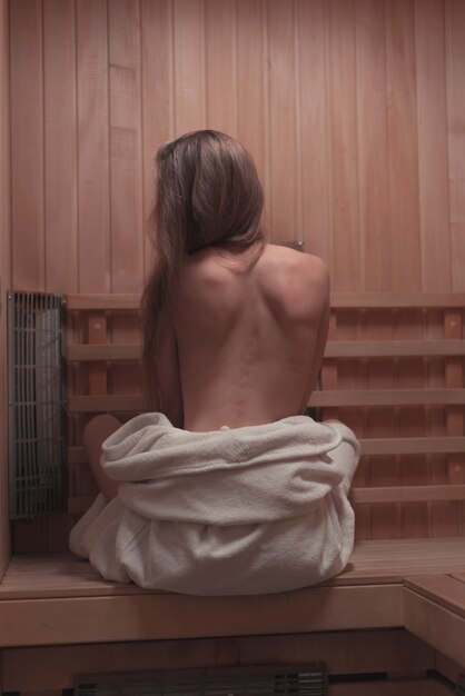 Backless sexy jonge vrouwenzitting op bank in sauna