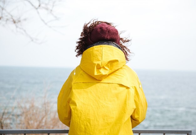 Backview schot van vrouw die weg op zee in gele regenjas kijkt