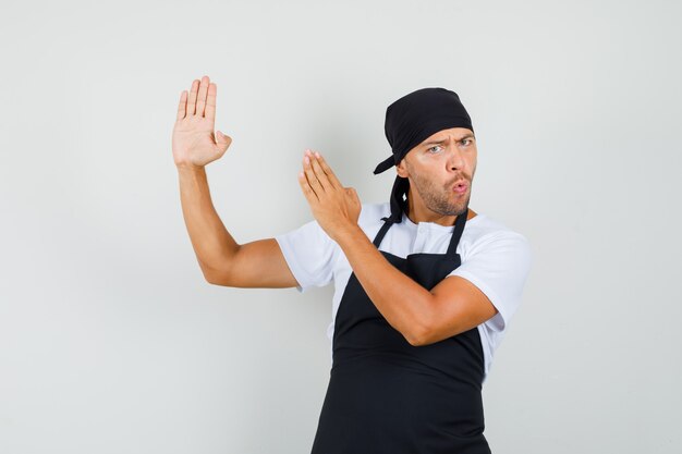 Baker man in t-shirt, schort met karate hakken gebaar en op zoek zelfverzekerd