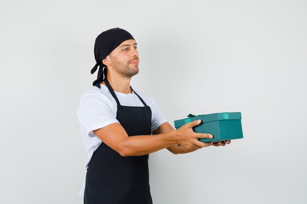 Baker man in t-shirt, schort presenteert geschenkdoos en ziet er vrolijk uit