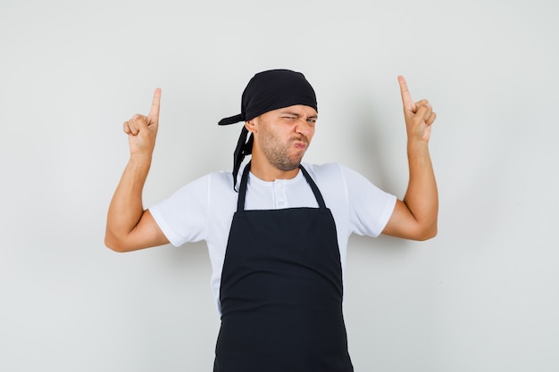 Baker man in t-shirt, schort vingers omhoog en fronsend