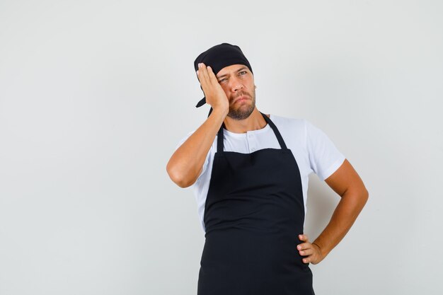 Baker man opzoeken in t-shirt, schort en peinzend kijken