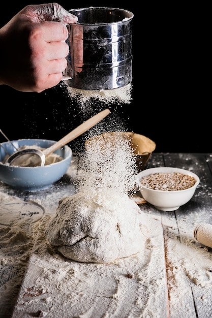 Baker&#39;s hand verschuift bloem met zeef op brooddeeg