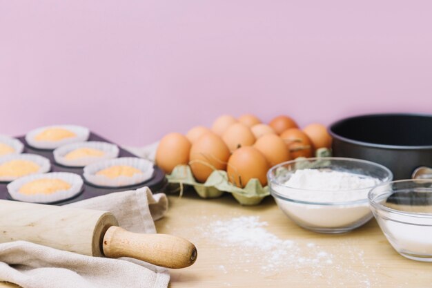 Bakkend cupcake ingrediënten met deegrollen op keuken worktop tegen roze achtergrond