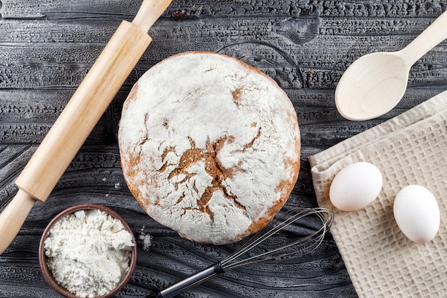 Bakkerijproduct met deegrol, bloem, eieren bovenaanzicht op een grijze houten oppervlak