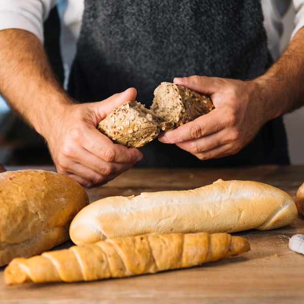 Gratis foto bakkers hand breekt volkoren brood over het houten bureau