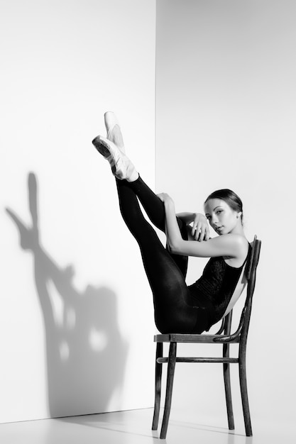 Ballerina in zwarte outfit poseren op een houten stoel, studio.