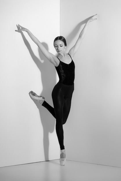 Ballerina in zwarte outfit poseren op pointe-schoenen, studio achtergrond.