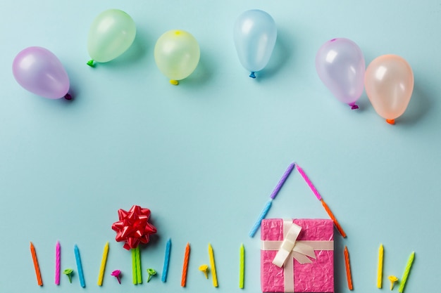 Ballonnen boven het huis gemaakt met geschenkdoos; kaarsen en rood lint buigen tegen blauwe achtergrond