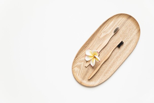Bamboe tandenborstel op een tafel met kopieerruimte op een witte achtergrond Gestileerde compositie van plat leggen met tropische bloemen