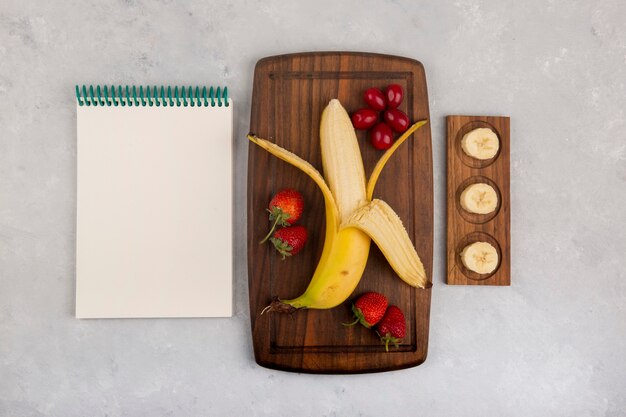 Banaan, aardbei en bessen op een houten schaal met een ontvangstboekje opzij