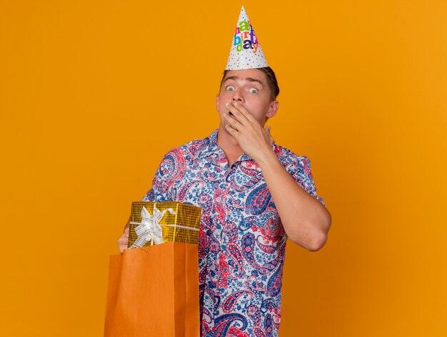 Bang jonge partij kerel dragen verjaardag glb bedrijf geschenk tas en bedekt gezicht met hand geïsoleerd op oranje
