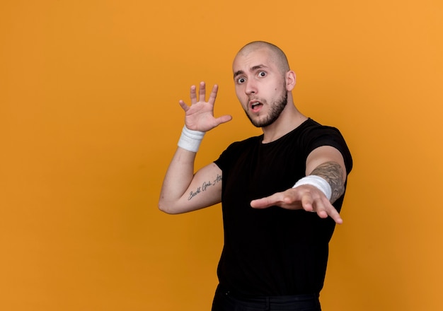 Bang jonge sportieve man met polsbandje hand standhouden geïsoleerd op oranje muur met kopie ruimte