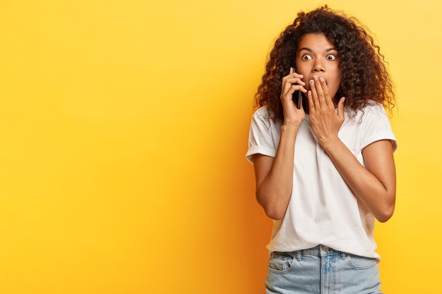 Bang jonge vrouw met krullend haar poseren met haar telefoon