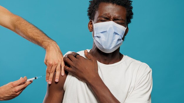 Bang persoon met gezichtsmasker die wordt ingeënt tegen coronavirus. Handen van arts met spuit die jonge man vaccineert met beschermend masker. Volwassene bang voor naald en vaccinatie.