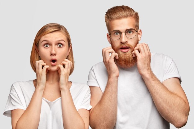 Bang vrouwen en mannen staren met afgeluisterde ogen, kijken bang, merken of horen iets slechts, gekleed in casual witte t-shirts, handen op de wangen. Collega's maken zich zorgen over het missen van de deadline.